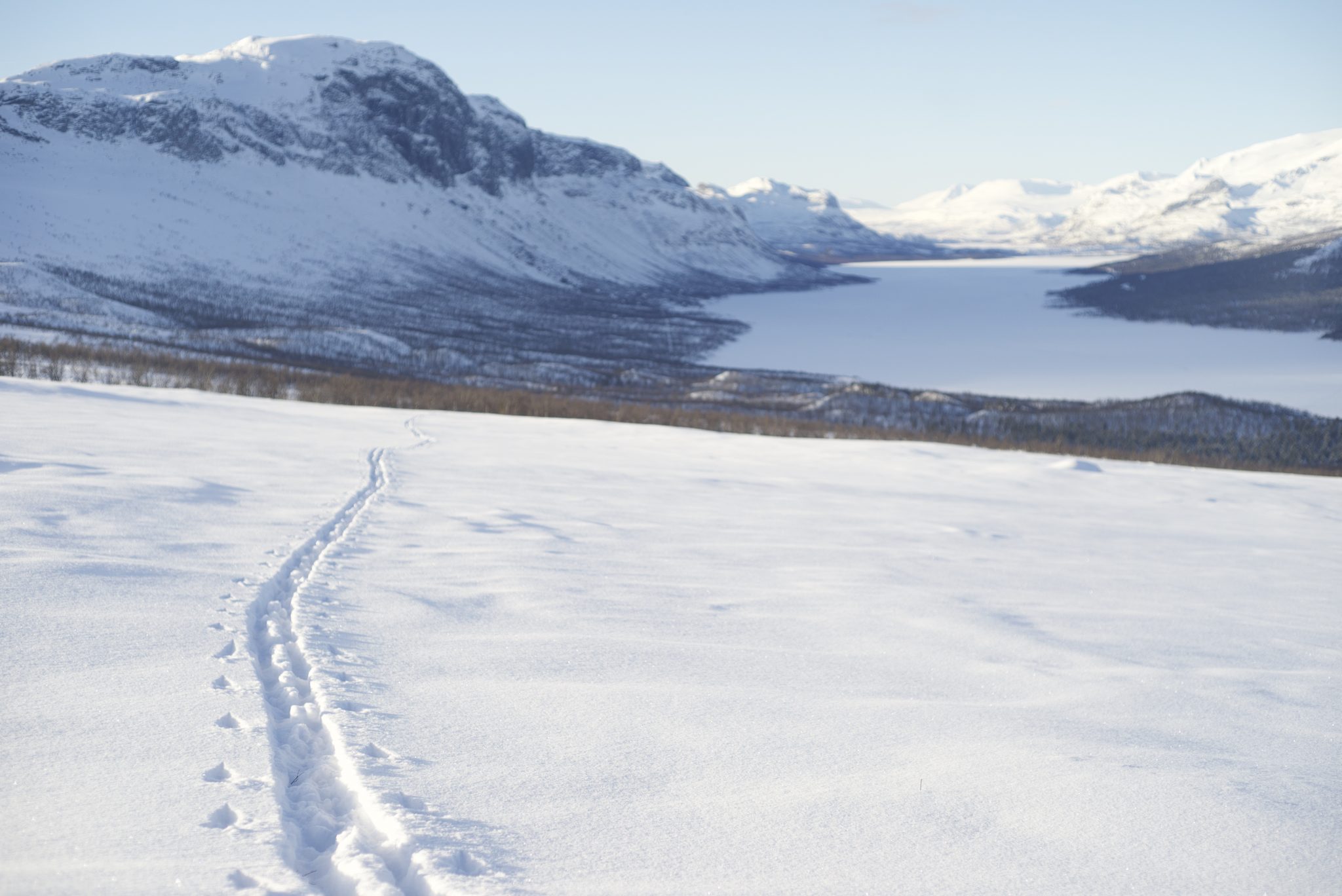 A trail in snow with mountains on the backround