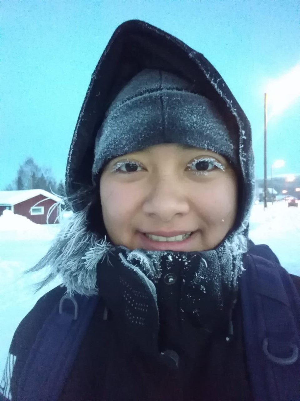 A young woman in winter clothing smiles at the camera, her face covered in frozen snow.