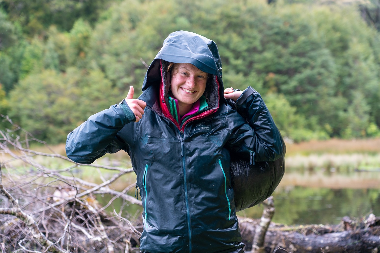 A woman in a raincoat is smiling and showing thumbs up