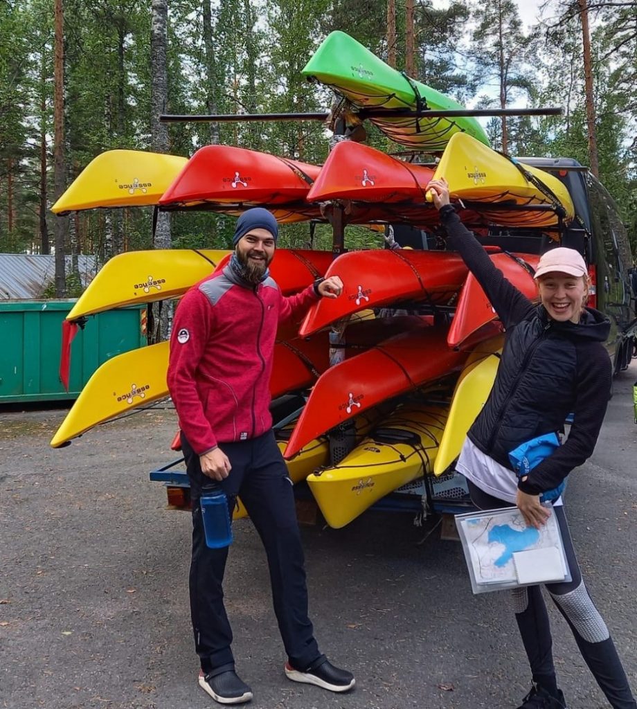 A man and a woman smiling while happily posing in front of a bunch of yellow, red, and green kayaks.