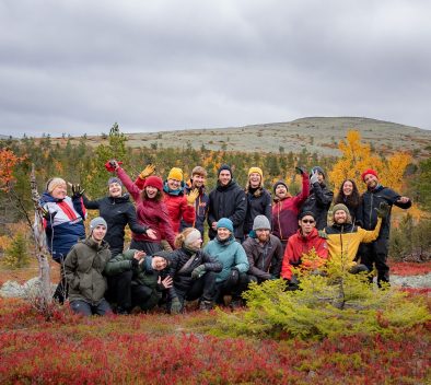 The 2021 class of adventure educators posing in Lapland surrounded by autumn foliage.