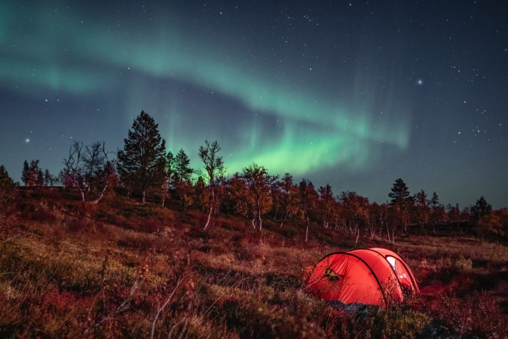 The northern lights in the night sky over a single red tent.