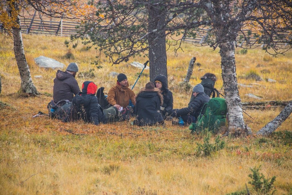 Six people dressed in hiking gear sitting under a tree in autumnal Ylläs.